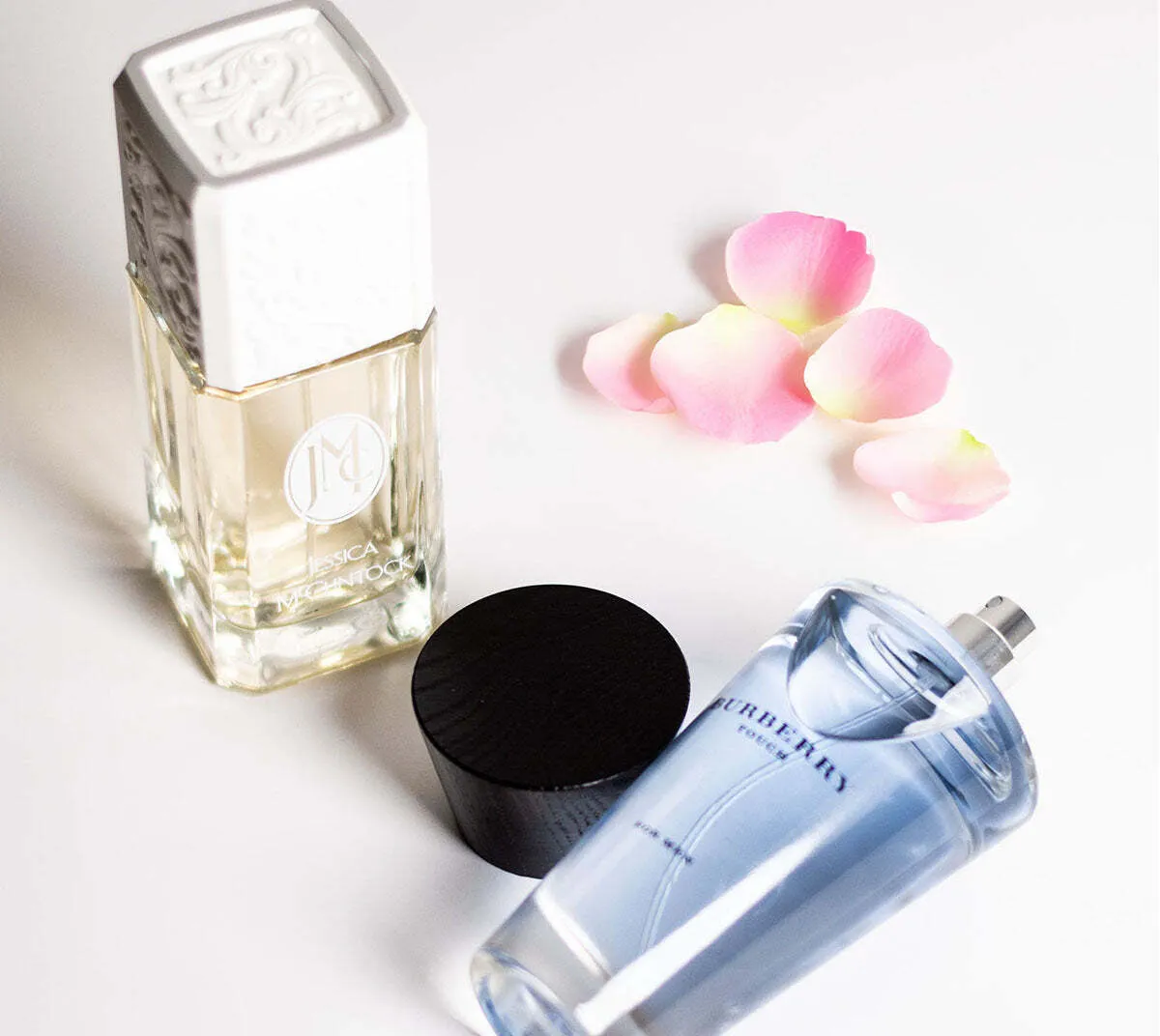 Jessica McClintock and Burberry Touch perfume bottles displayed on a white surface with scattered pink rose petals.