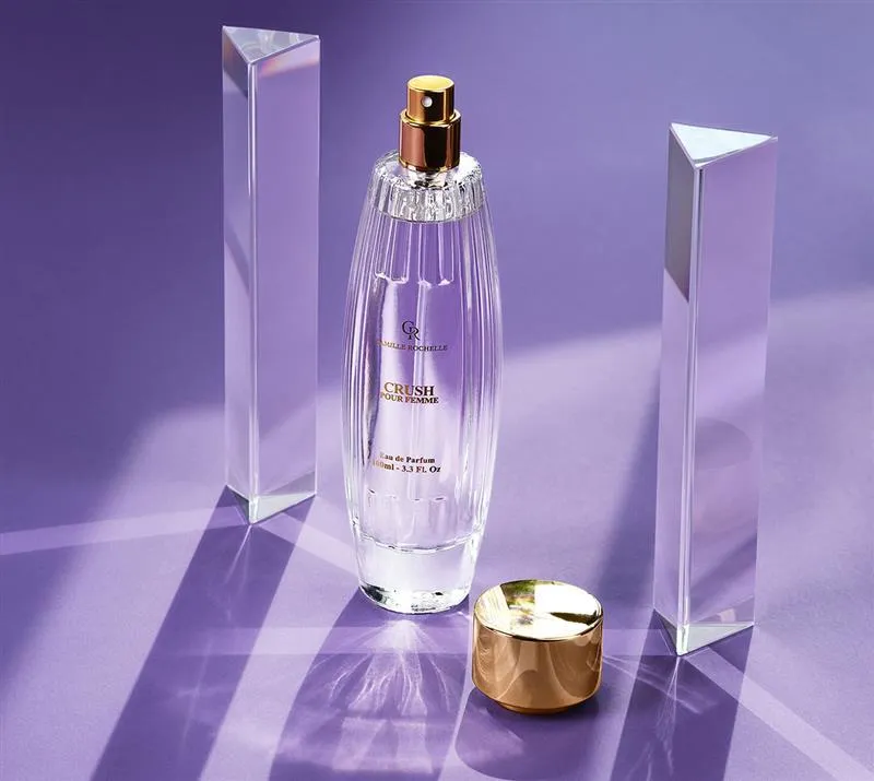 Camille Rochelle Crush Pour Femme perfume bottle with a gold cap, displayed on a purple background with crystal prisms.