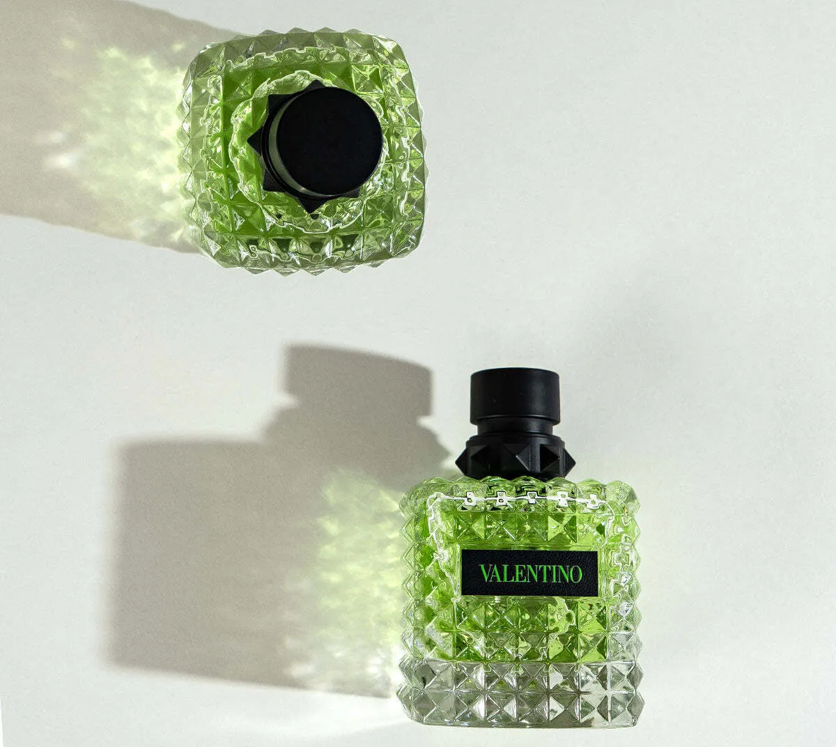 Valentino perfume bottle with green liquid in a studded glass design, shown upright and reflected from above.