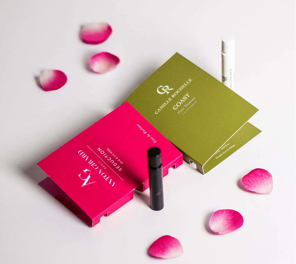 Camille Rochelle perfume discovery set with sample vials, pink and green packaging, and scattered rose petals on a white background.